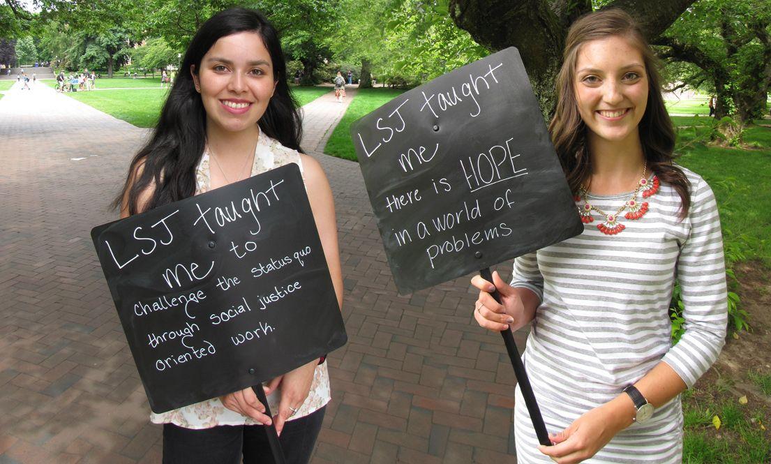 Two LSJ students in the UW Quad holding signs reading 'LSJ taught me to challenge the status quo through social justice oriented worth' and 'LSJ taught me there is HOPE in a world of problems.'
