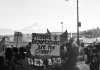 Black and white photo of protestors. In the center is a sign or poster that says "Prisons& deportations are the crime!"